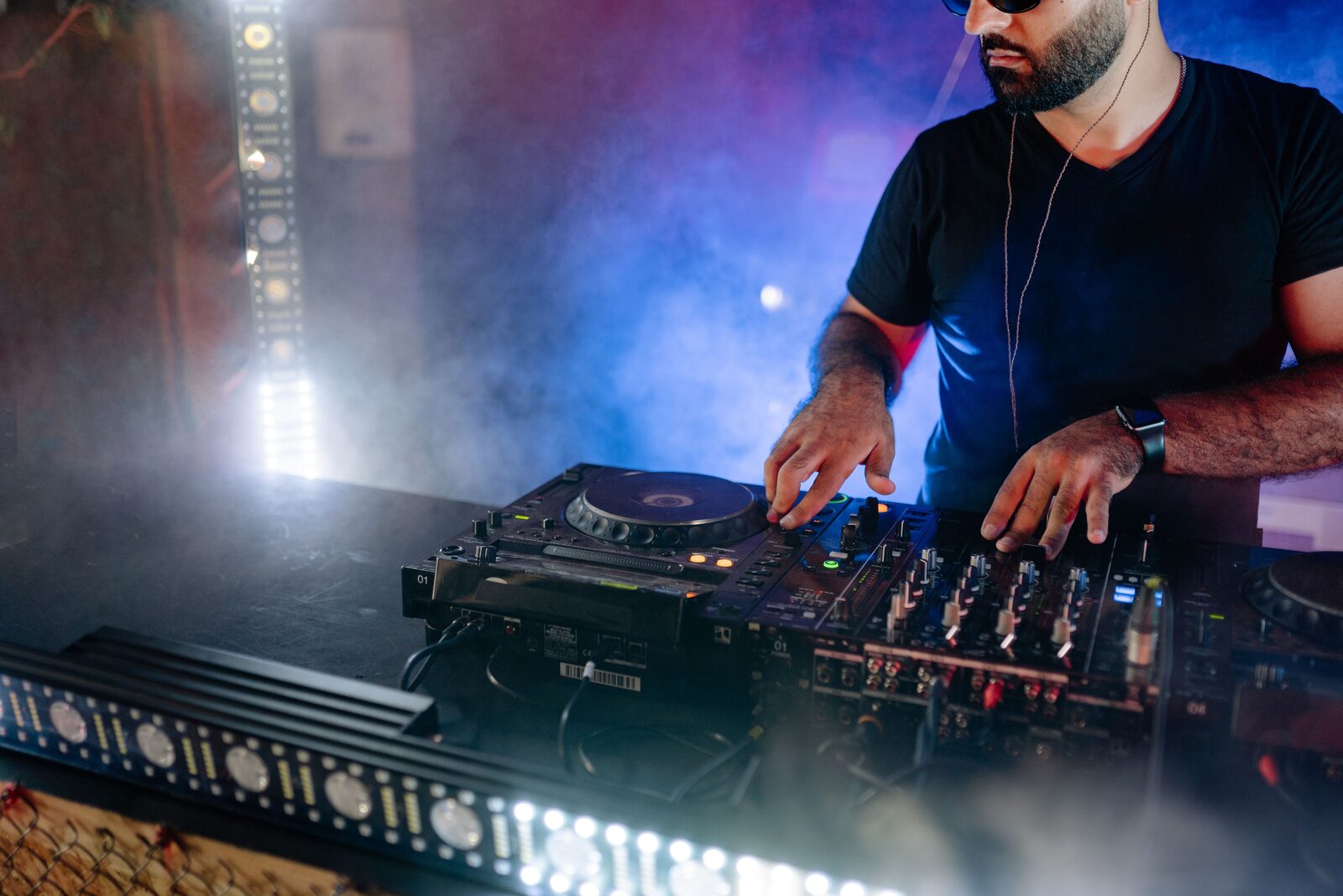 A DJ working a mixer and deck controls behind a lit booth at an evening event