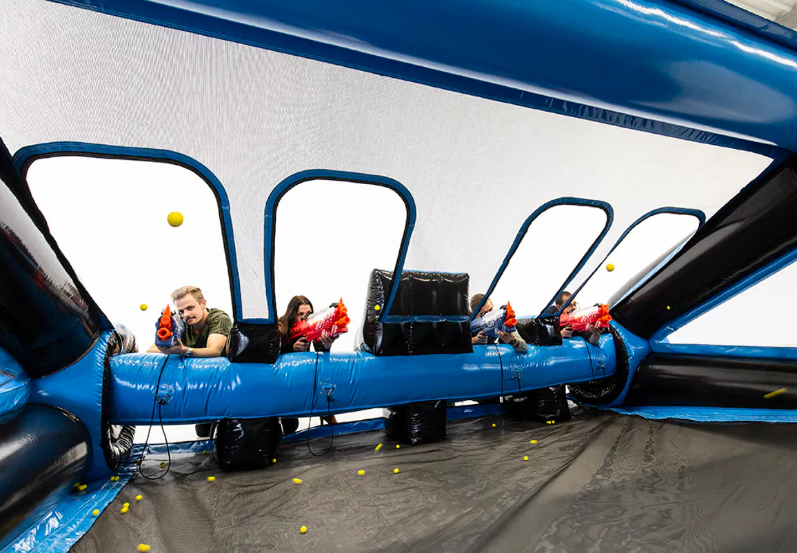Four adults using soft foam-ball blasters inside the IPS Shooting Gallery