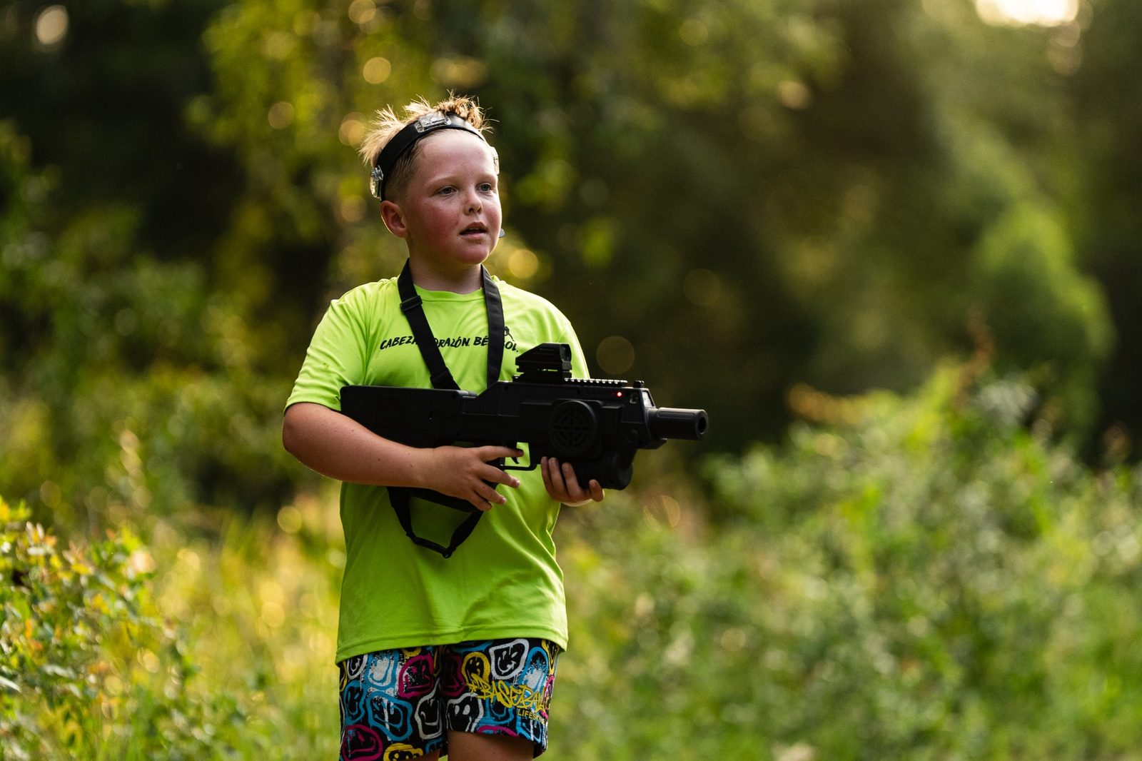 Young player in a bright green shirt holding a laser tagger outdoors