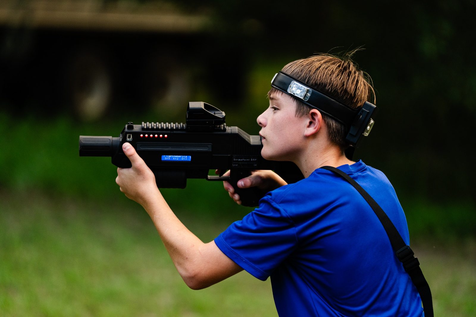 Young player in a blue shirt aiming a laser tagger outdoors