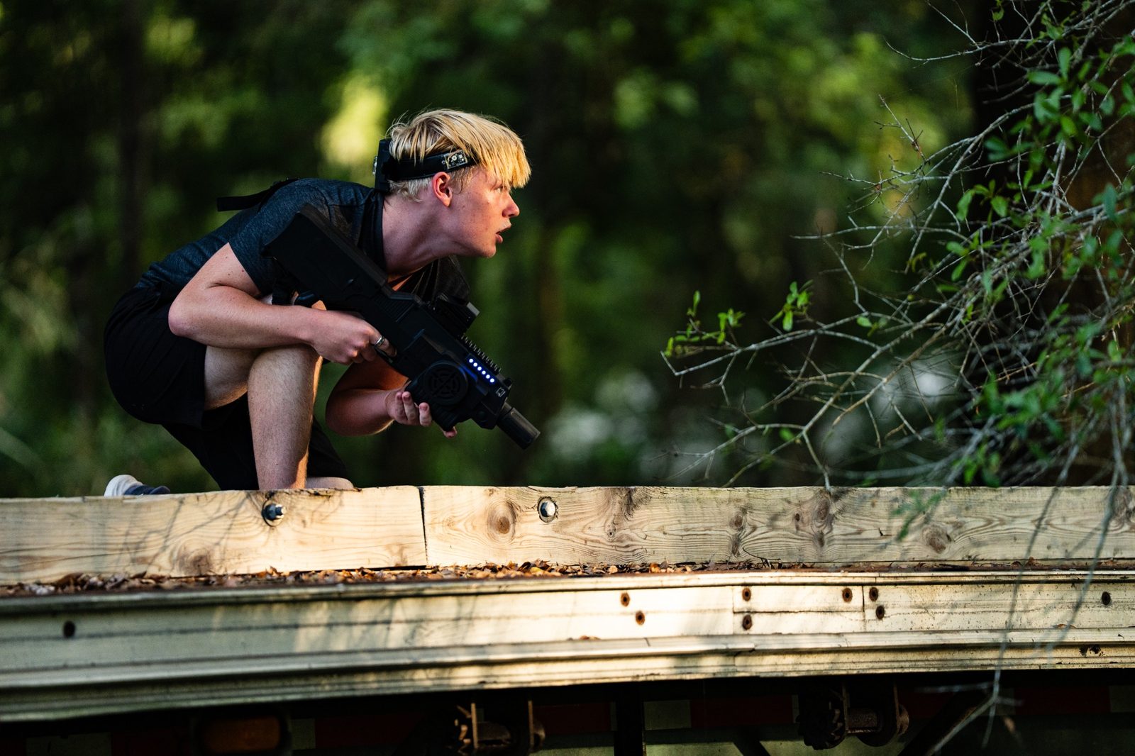 Player crouching behind cover with a laser tagger on an outdoor course