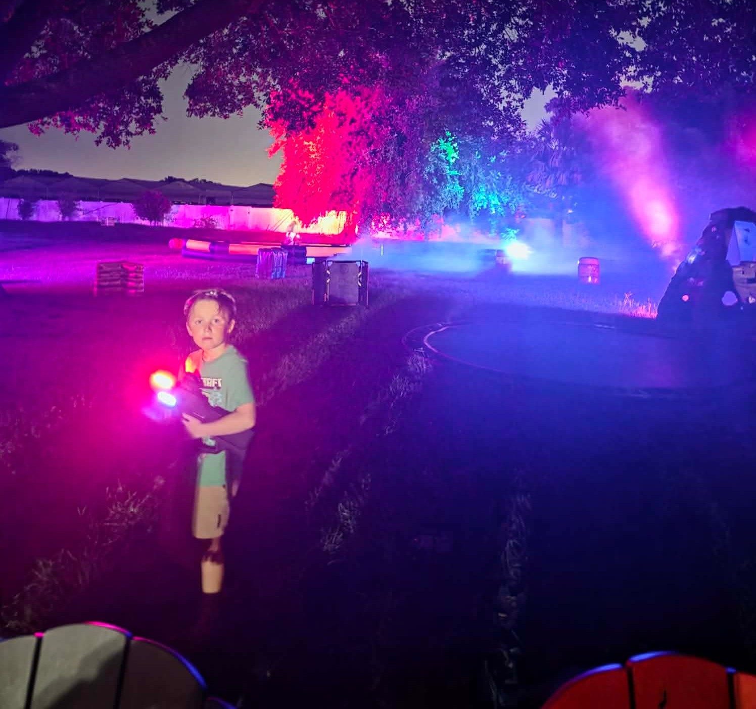 Young player holding illuminated laser-tag equipment on a colorful nighttime field